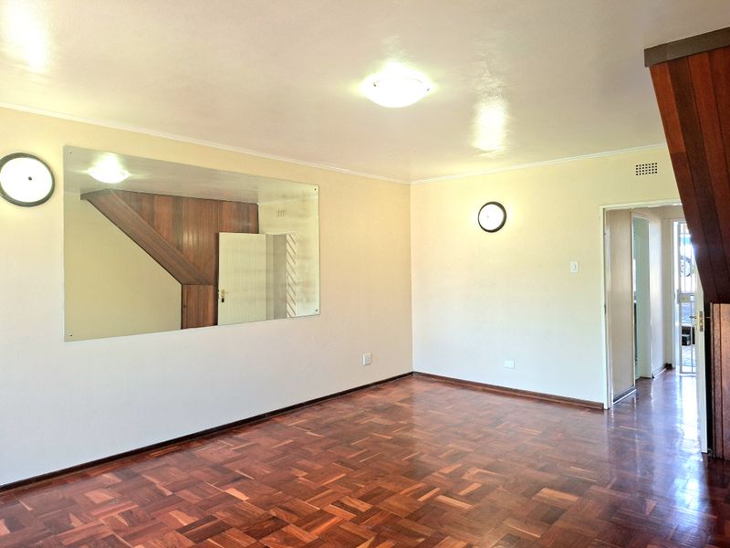Spacious living area featuring classic parquet flooring, a large wall-mounted mirror, and timber staircase detailing, offering a blank canvas for interior design.