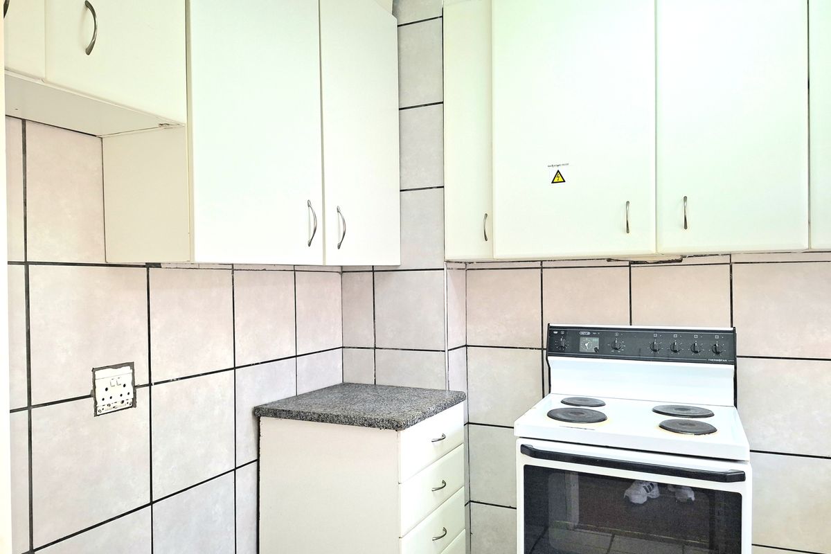 A compact kitchen featuring white built-in cabinetry, a tiled splashback, and a freestanding electric stove.