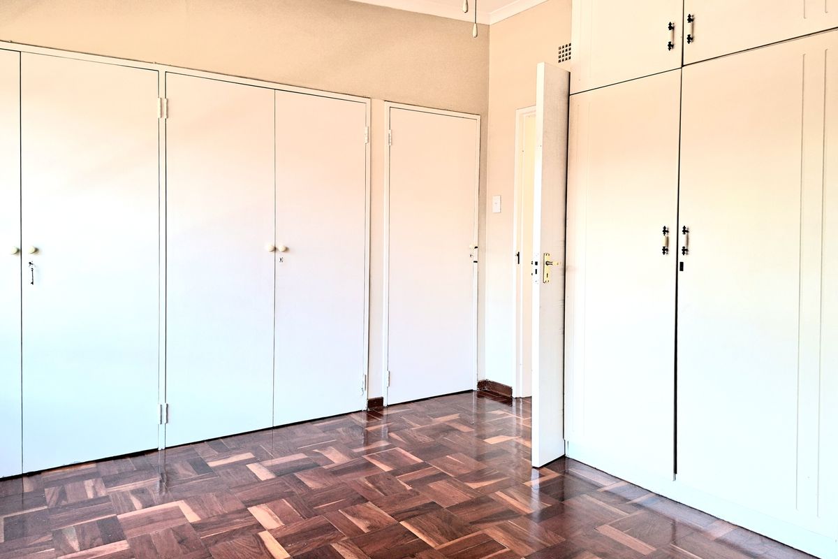 A bright, empty bedroom featuring classic parquet flooring and extensive built-in cupboard storage with overhead cabinetry.