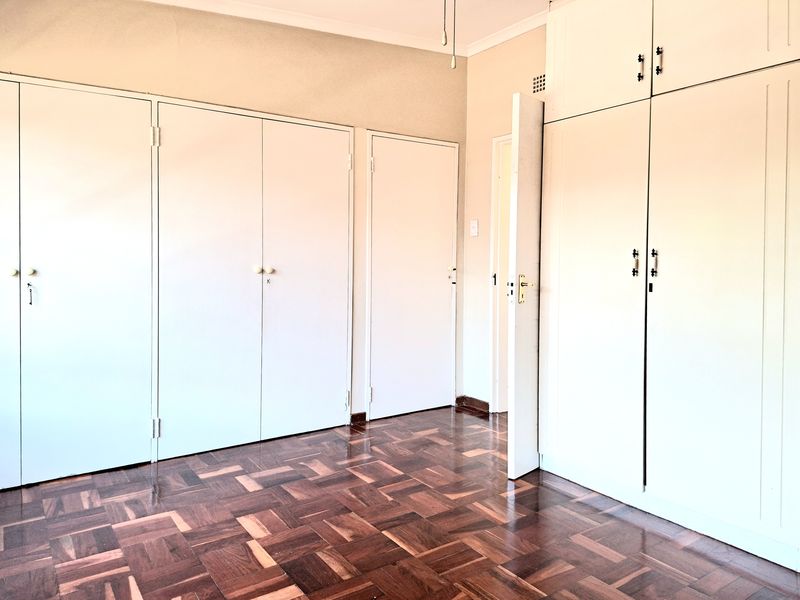 A bright, empty bedroom featuring classic parquet flooring and extensive built-in cupboard storage with overhead cabinetry.
