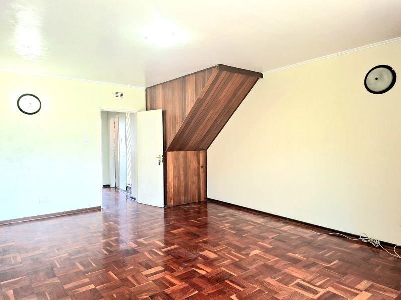 An empty living room featuring classic parquet flooring and a distinctive wood-paneled feature wall, offering a blank canvas for interior design.
