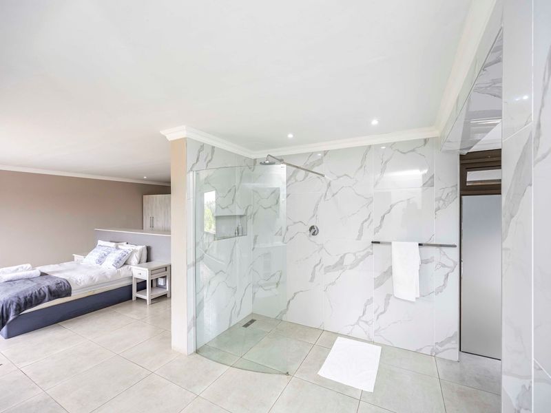 Modern open-plan bedroom featuring an integrated walk-in shower with marble-look tiling, glass screen, and contemporary finishes.