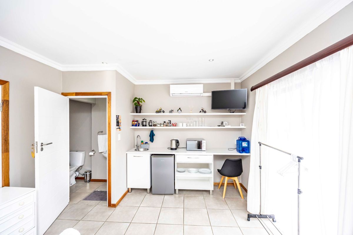 A compact kitchenette featuring built-in cabinetry, a sink, floating shelves, and an air conditioning unit, with an adjacent bathroom entrance.