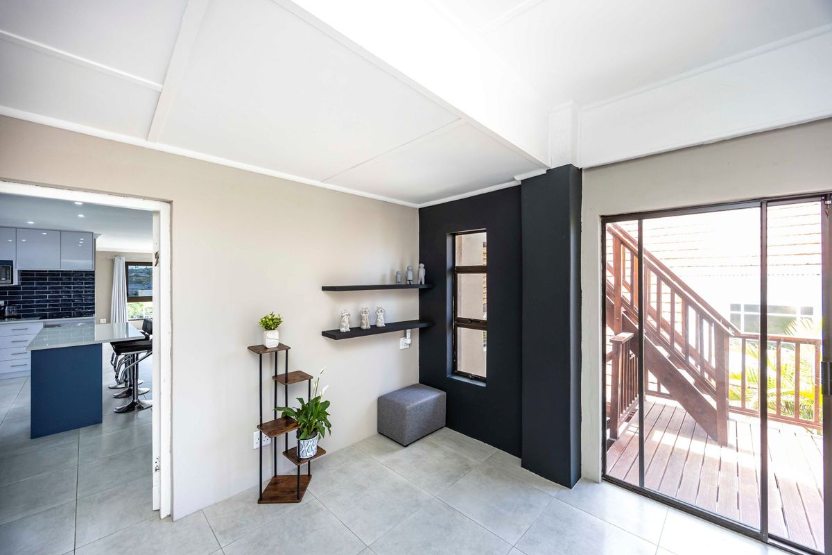 A bright living area featuring tiled floors, a sliding door leading to an outdoor staircase, and a view into the adjacent modern kitchen.