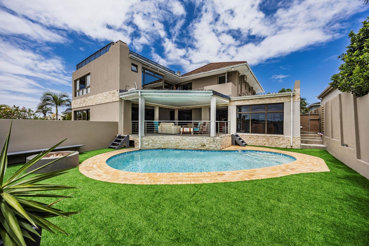 Rear view of a multi-story house featuring a swimming pool, covered patio, fire pit area, and landscaped artificial lawn.
