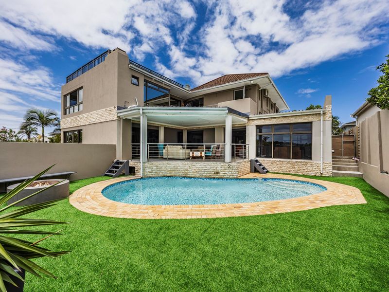 Rear view of a multi-story house featuring a swimming pool, covered patio, fire pit area, and landscaped artificial lawn.