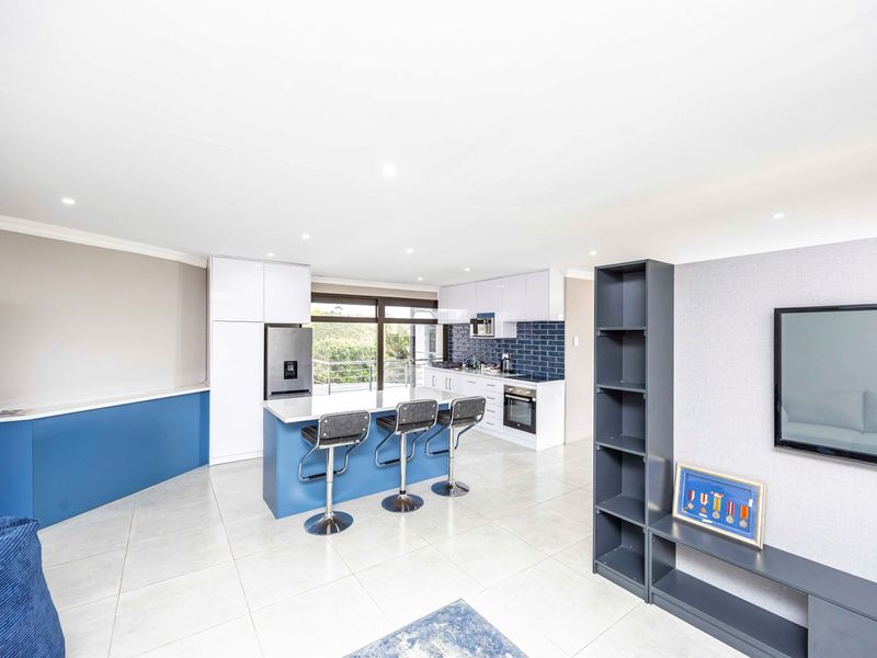 Modern open-plan living area featuring a contemporary kitchen with a central island, sleek cabinetry, subway tile backsplash, and direct access to an outdoor balcony.