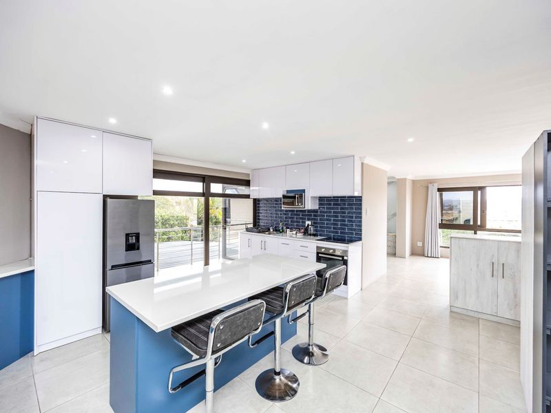 Modern open-plan kitchen featuring a central island, sleek white cabinetry, blue accents, subway tile backsplash, and direct access to an outdoor balcony.