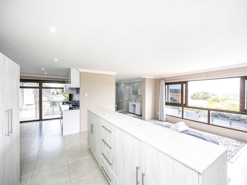 Spacious open-plan living area featuring modern built-in cabinetry, tiled floors, large windows with natural light, and an integrated kitchenette and en-suite bathroom.