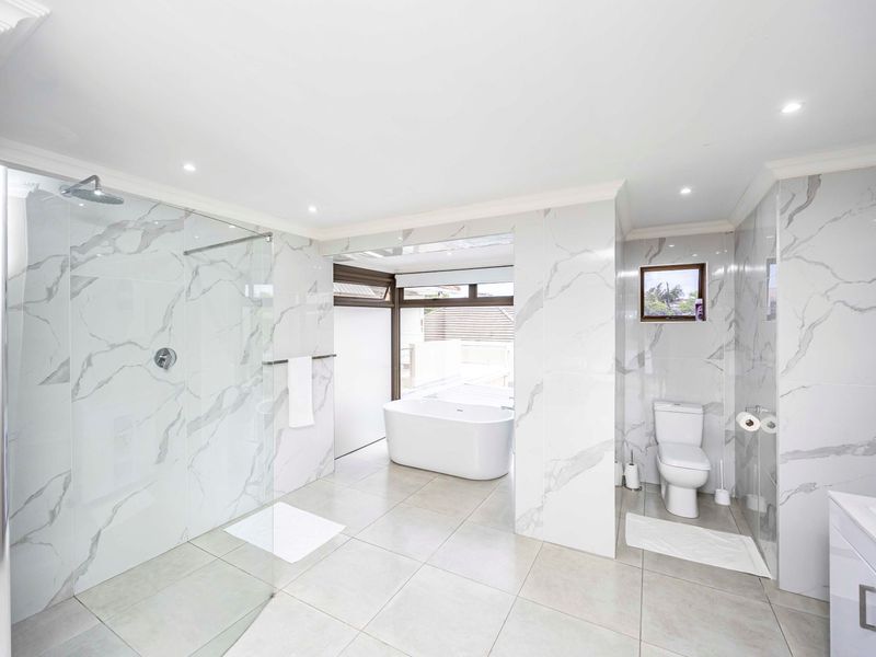 Modern, spacious bathroom featuring marble-look wall tiles, a large walk-in shower, a sleek freestanding bathtub, and high-quality finishes throughout.