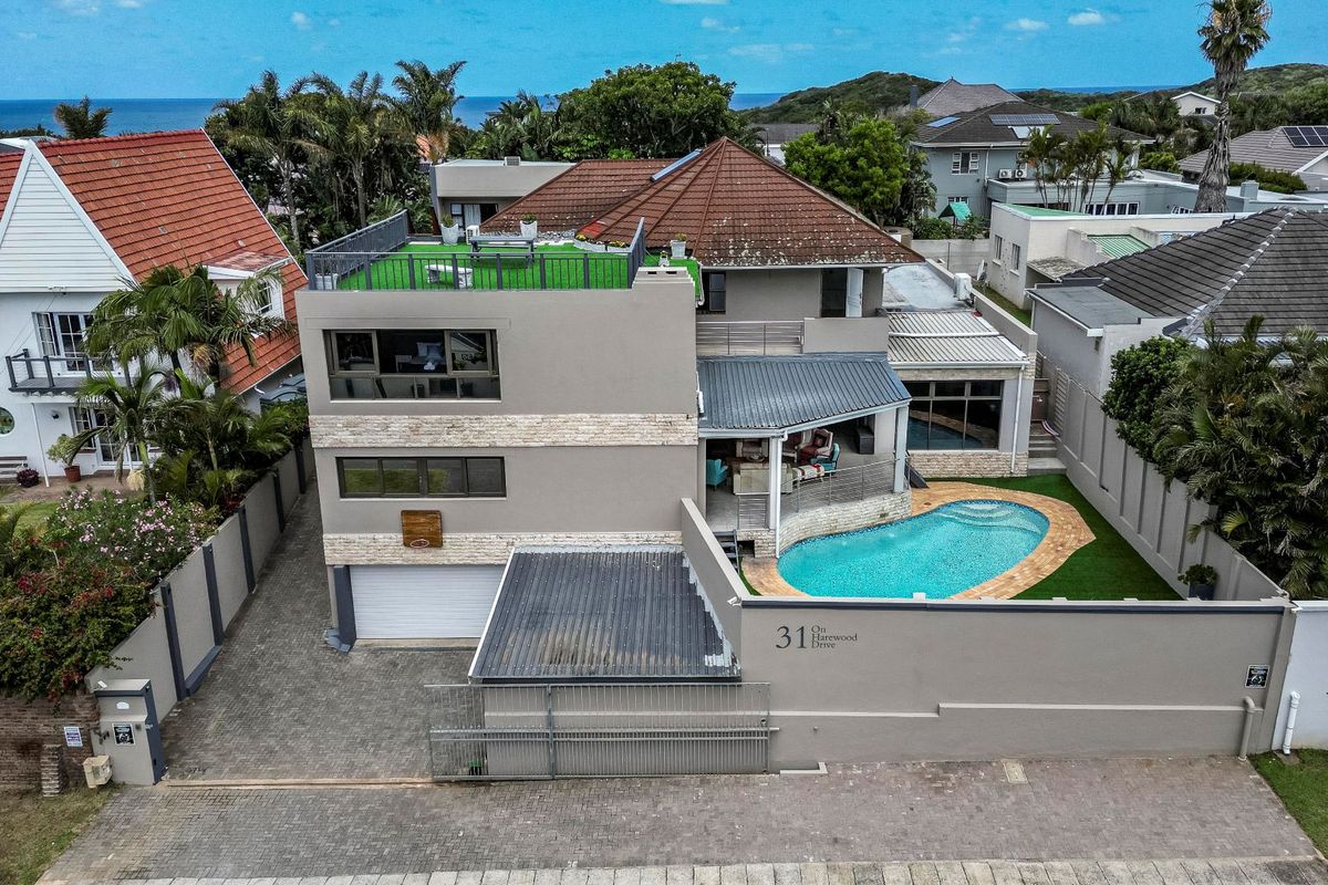 Aerial view of a multi-level residential property featuring a swimming pool, rooftop terrace, paved driveway, and secure boundary walling.