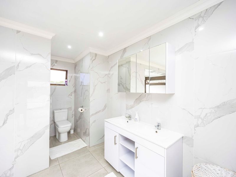Modern bathroom featuring a double vanity with a mirrored cabinet, marble-look wall tiling, and a private toilet area with recessed lighting.