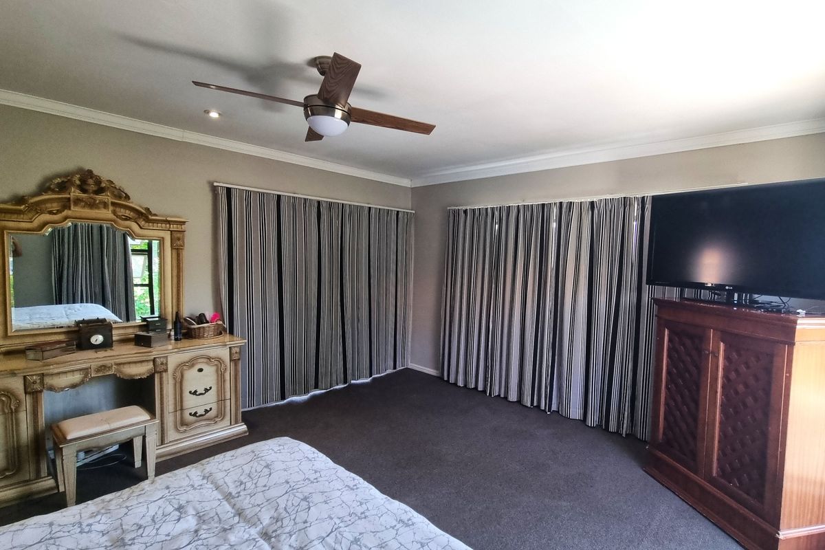 Spacious bedroom featuring neutral wall tones, carpeted flooring, a ceiling fan, and large windows covered by floor-to-ceiling curtains.
