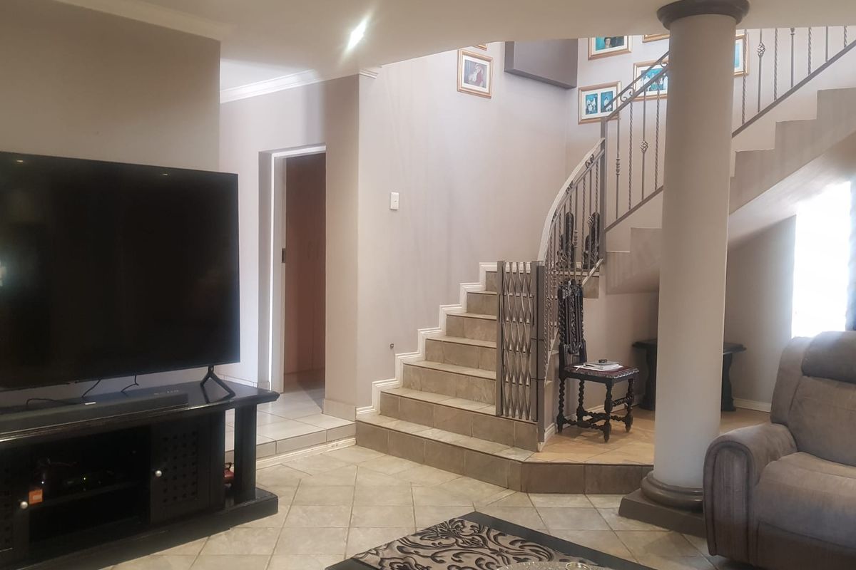 A living area featuring tiled flooring, a central structural column, and a staircase with a decorative wrought iron balustrade.