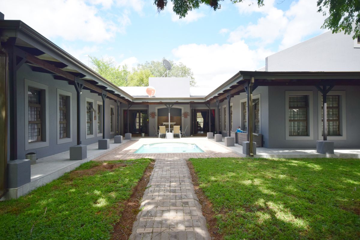 A U-shaped rear courtyard featuring a central swimming pool, paved walkway, and covered patio areas surrounding a landscaped garden.