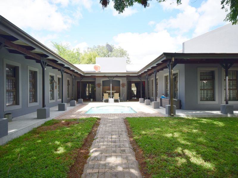 A U-shaped rear courtyard featuring a central swimming pool, paved walkway, and covered patio areas surrounding a landscaped garden.