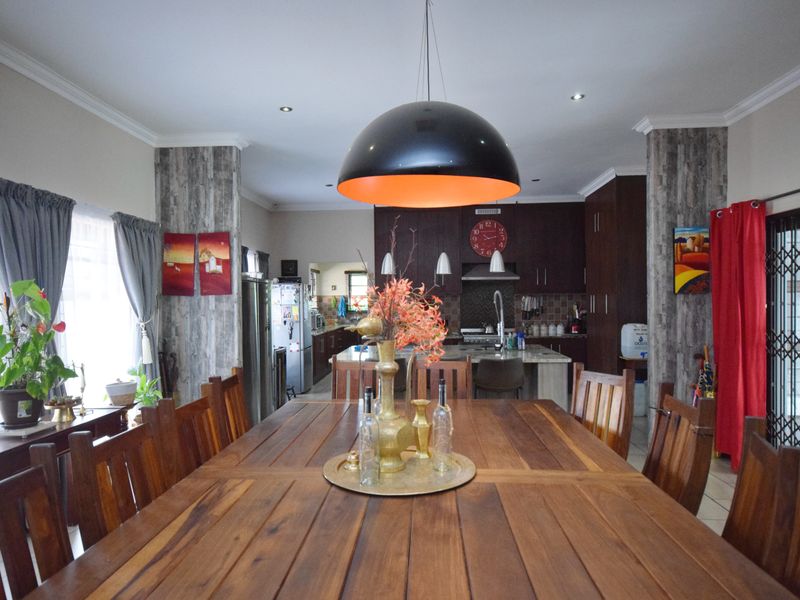 Spacious open-plan dining and kitchen area featuring dark wood cabinetry, a central kitchen island, and modern pendant lighting.