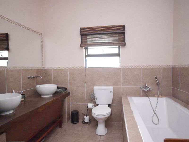 A functional bathroom featuring a double vessel sink vanity, a standard toilet, and a bathtub with a handheld shower mixer.
