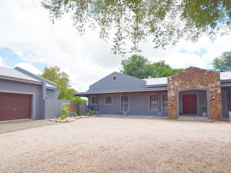 Front view of a modern house featuring a stone-clad entrance, grey exterior walls, metal roofing, and a spacious gravel driveway with an attached double garage.