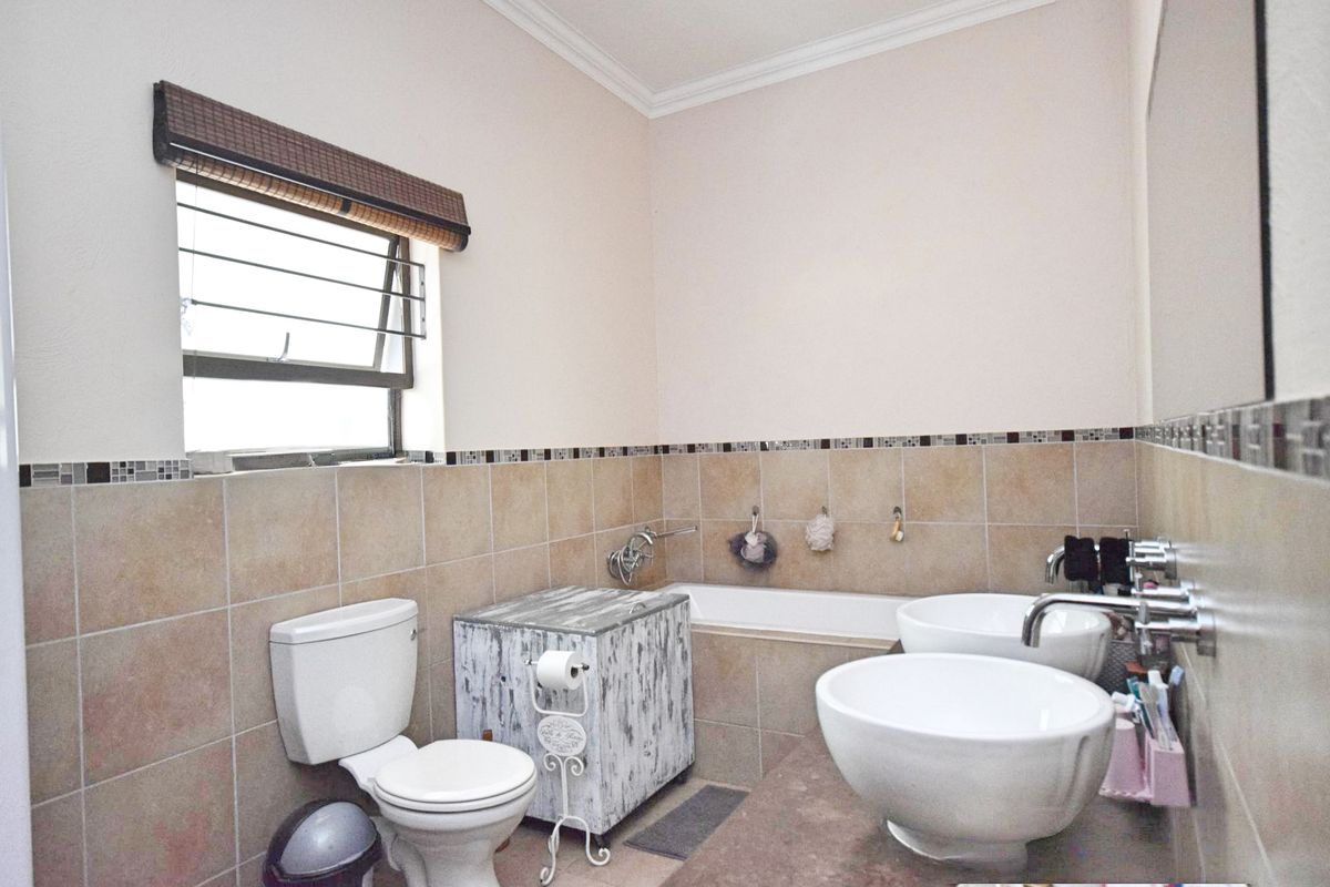 A functional bathroom featuring dual vessel sinks, a built-in bathtub, ceramic wall tiling with a mosaic border, and a top-hung window.