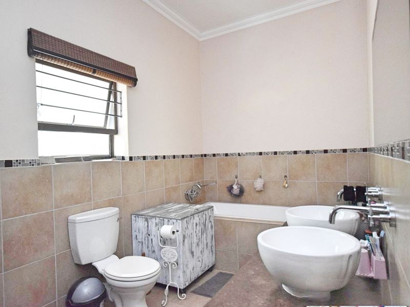A functional bathroom featuring dual vessel sinks, a built-in bathtub, ceramic wall tiling with a mosaic border, and a top-hung window.