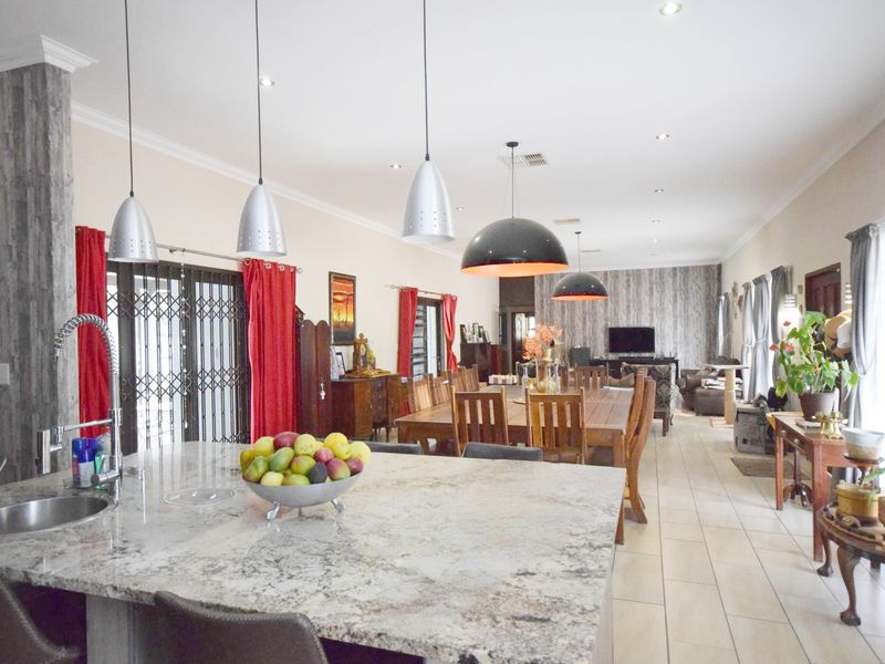Spacious open-plan living, dining, and kitchen area featuring a large granite island, modern pendant lighting, and neutral tiled flooring throughout.