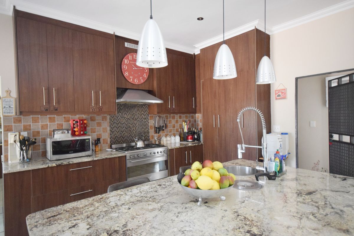 A well-appointed kitchen featuring dark wood cabinetry, granite countertops, a central island with a prep sink, and stainless steel appliances.