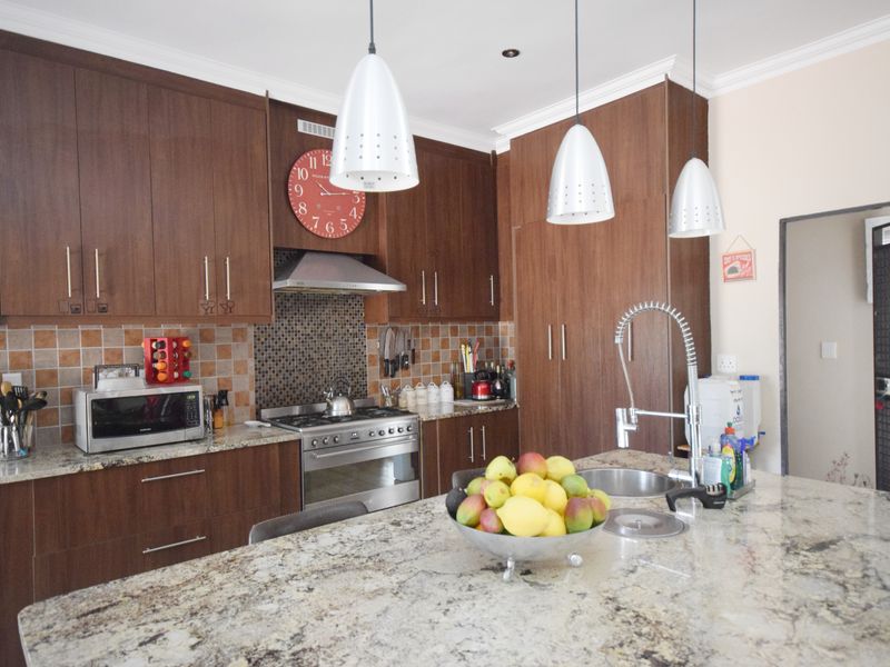A well-appointed kitchen featuring dark wood cabinetry, granite countertops, a central island with a prep sink, and stainless steel appliances.