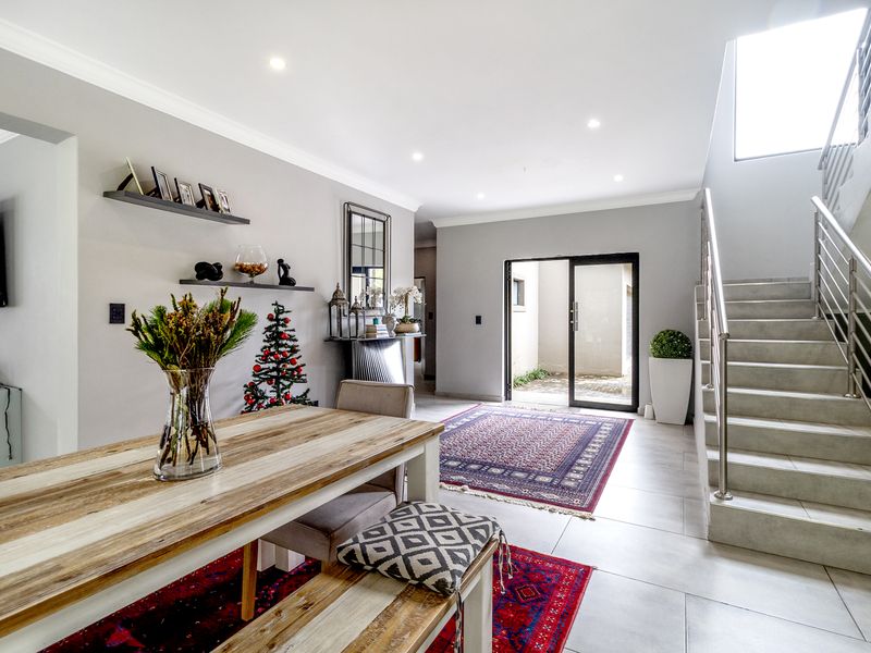 Open-plan living area featuring tiled flooring, recessed lighting, and a modern staircase with a stainless steel balustrade leading to the upper level.