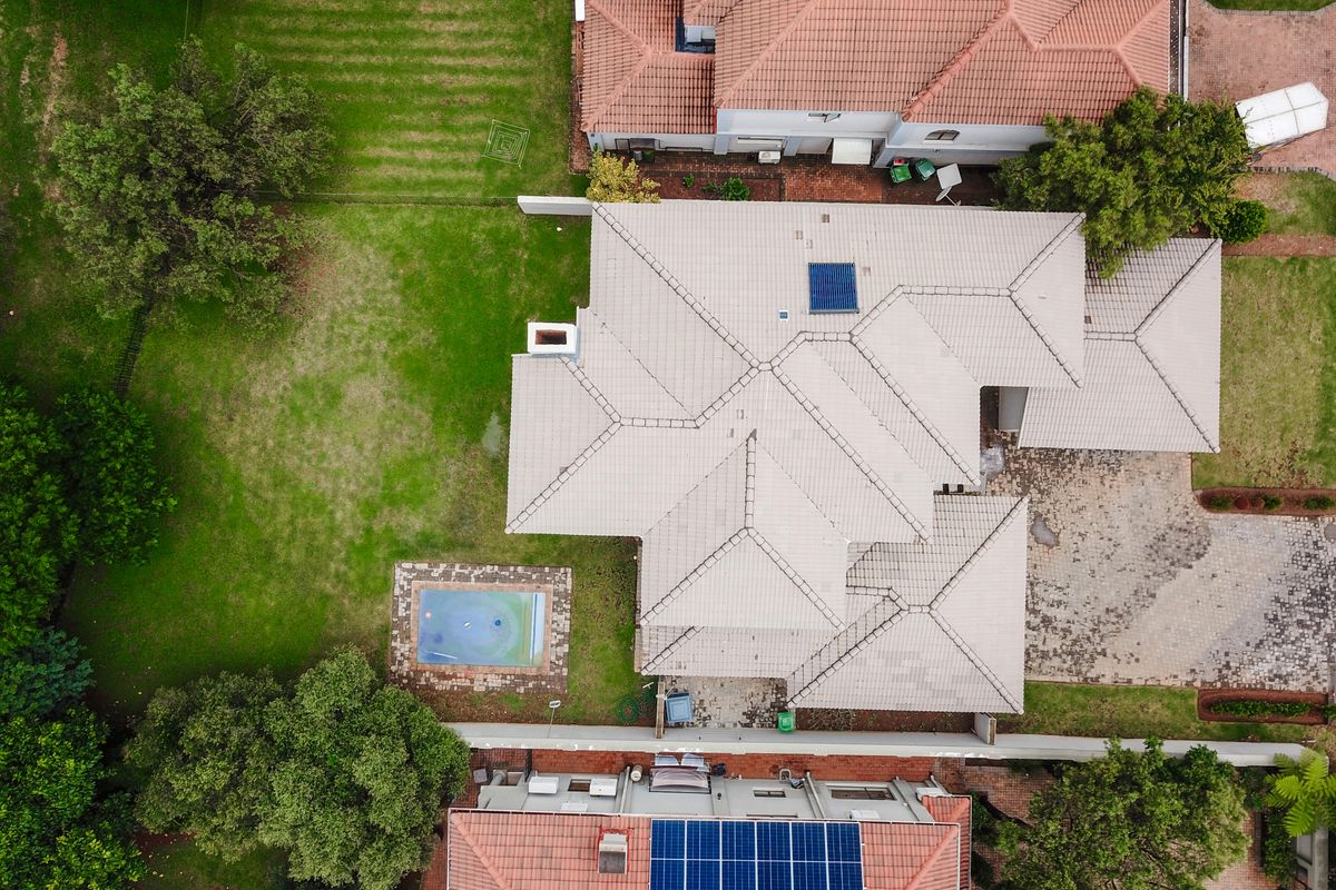 Aerial view of the property showcasing the tiled roof, swimming pool, solar panels, and surrounding garden area.