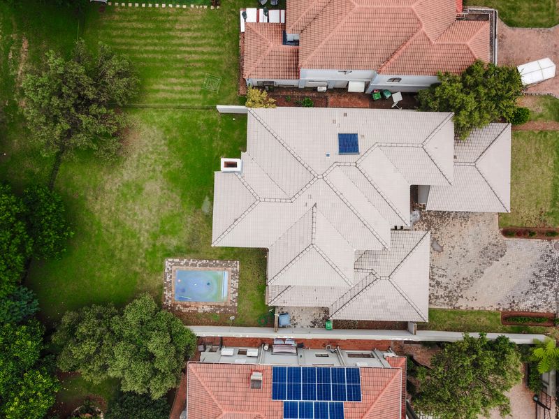 Aerial view of the property showcasing the tiled roof, swimming pool, solar panels, and surrounding garden area.