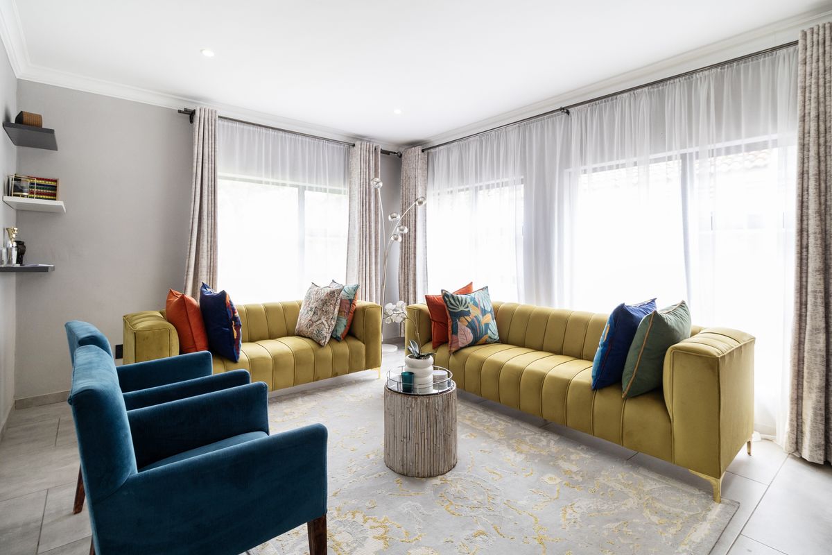 A bright and well-maintained living room featuring large windows with curtain tracks, recessed downlighting, and neutral tiled flooring.
