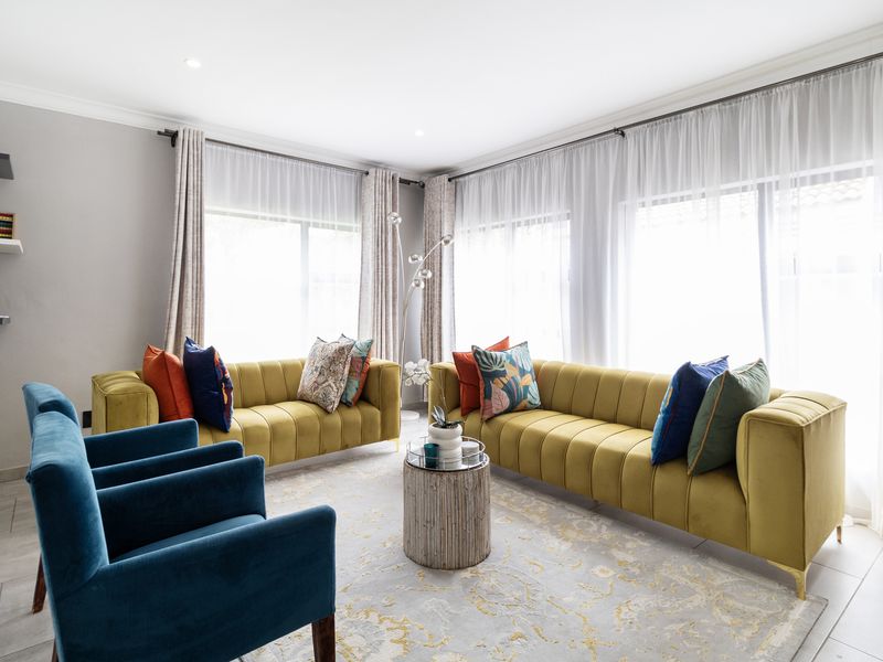 A bright and well-maintained living room featuring large windows with curtain tracks, recessed downlighting, and neutral tiled flooring.