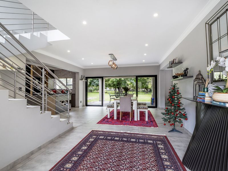 Spacious open-plan living and dining area featuring a modern staircase with stainless steel balustrades, recessed lighting, and large sliding doors opening to the garden.