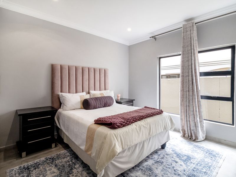 A well-maintained bedroom featuring built-in cupboards, neutral wall finishes, and large aluminium-framed windows allowing for natural light.
