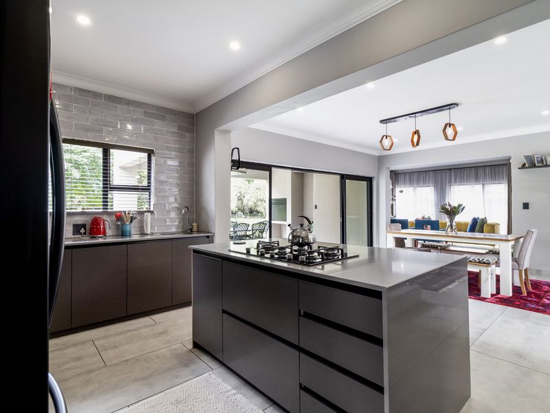 Modern open-plan kitchen featuring a central island with gas cooktop, sleek cabinetry, subway tile backsplash, and seamless flow to the adjacent dining area.