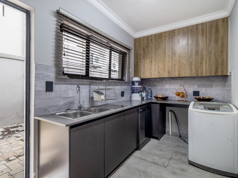 Functional laundry room featuring modern cabinetry, stainless steel double sink, tiled backsplash, and direct access to an outdoor paved area.