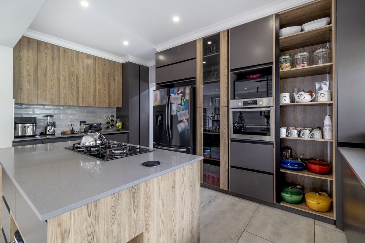 Modern kitchen featuring a central island with gas cooktop, sleek wood-tone and dark cabinetry, built-in appliances, and contemporary stone countertops.