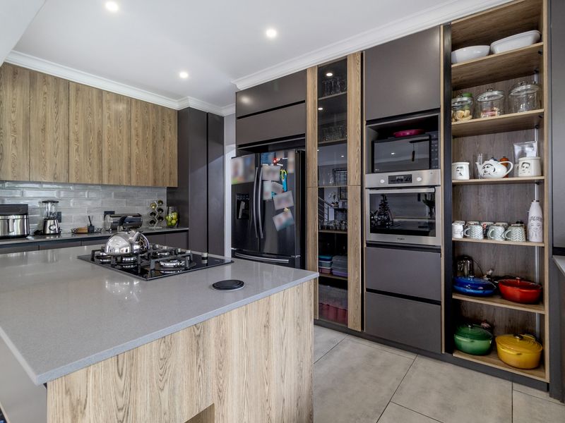 Modern kitchen featuring a central island with gas cooktop, sleek wood-tone and dark cabinetry, built-in appliances, and contemporary stone countertops.