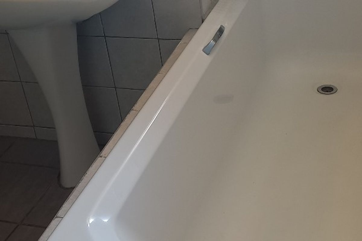 A functional bathroom featuring a pedestal washbasin and a built-in bathtub with tiled finishes throughout.