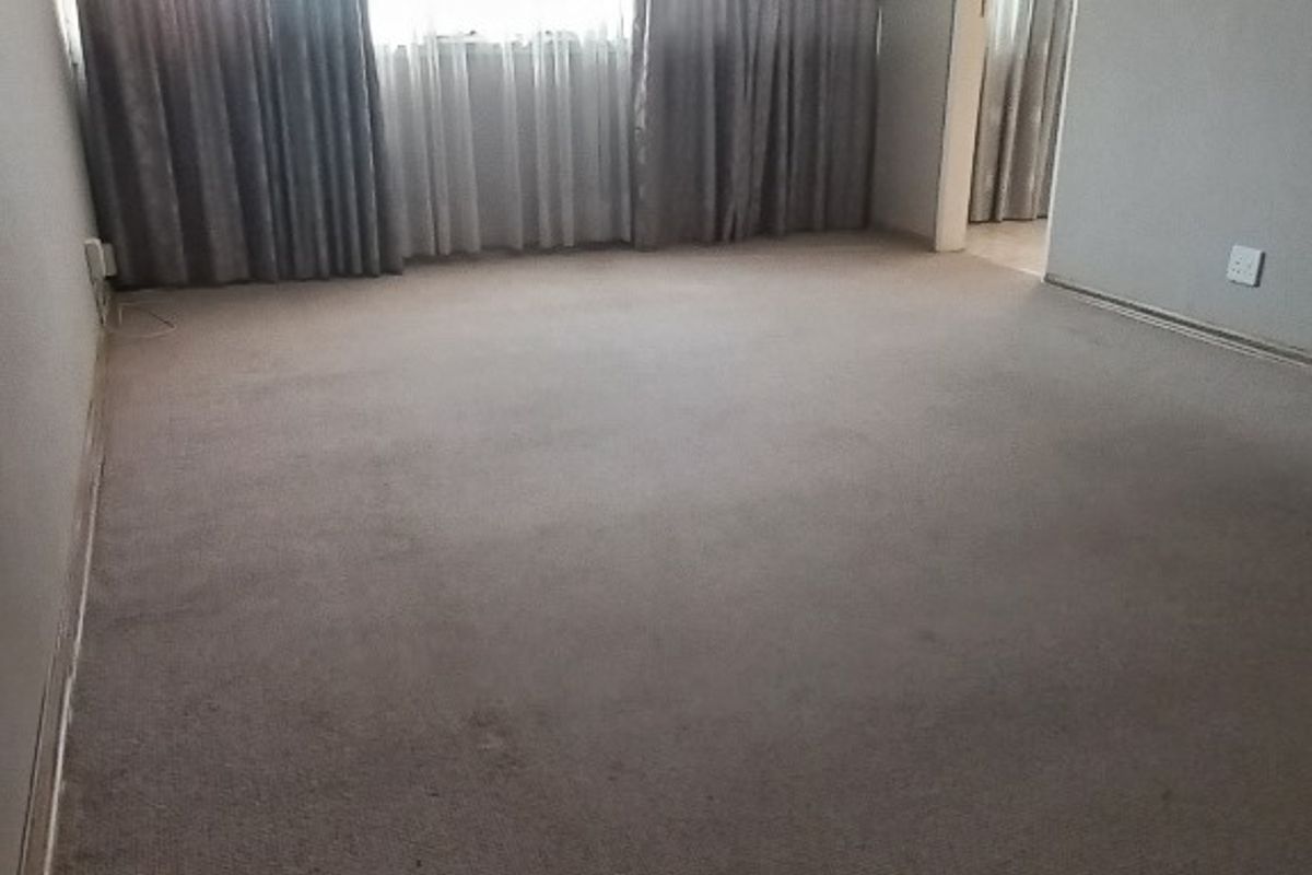 An empty living room featuring neutral wall finishes and carpet flooring, providing a blank canvas for potential interior design updates.