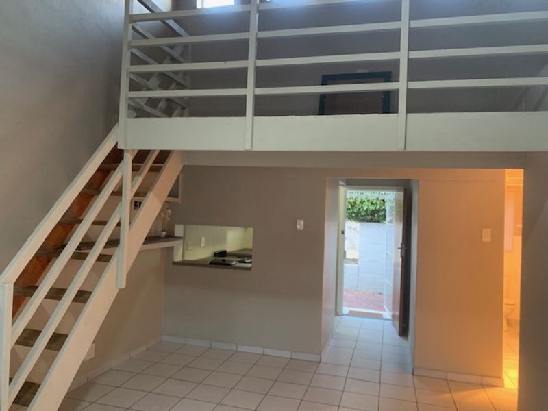 Open plan living area featuring a mezzanine level, timber staircase, tiled flooring, and direct access to an outdoor area.