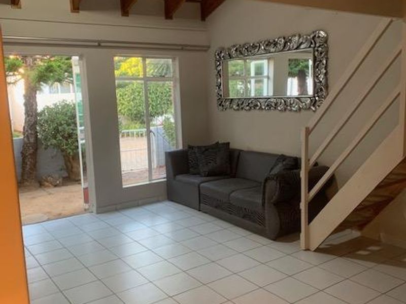 Open-plan living area featuring tiled flooring, exposed timber ceiling beams, and a staircase, with direct access to an outdoor patio area.