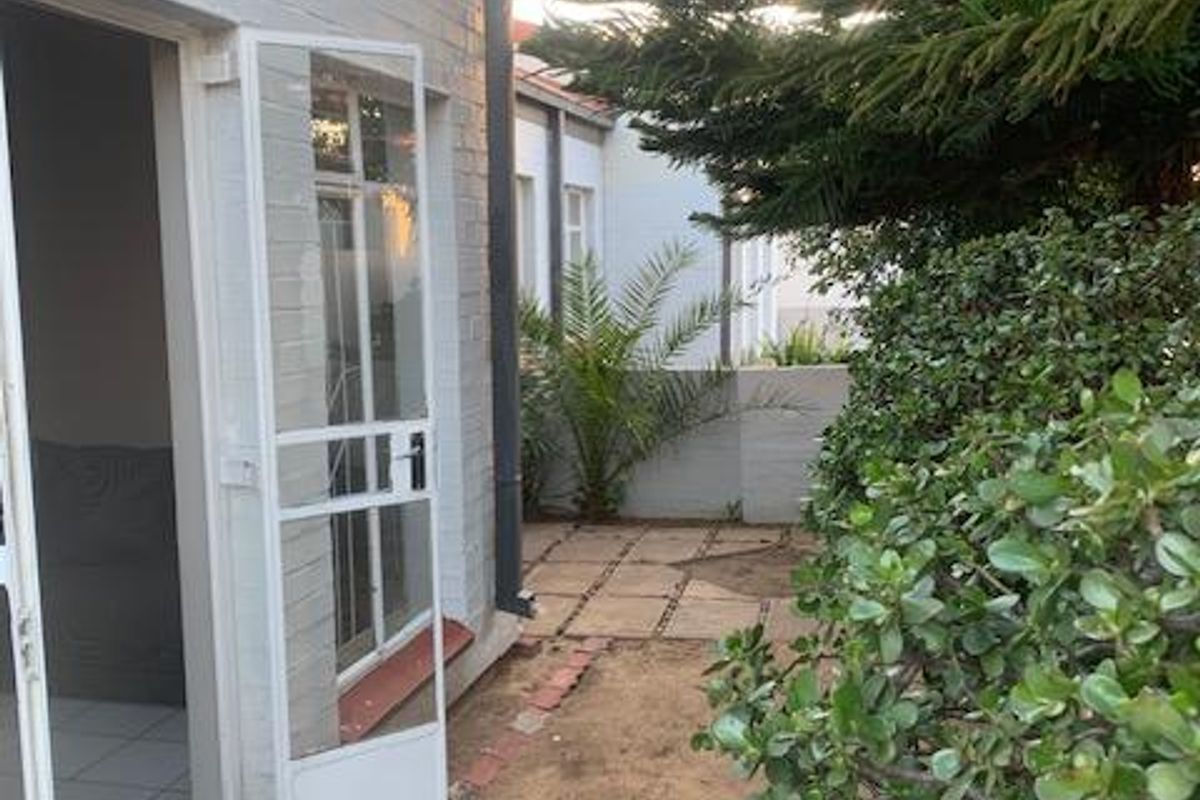 A view of the rear exterior area featuring a security gate, paved walkway, and established garden beds along the brick townhouse wall.