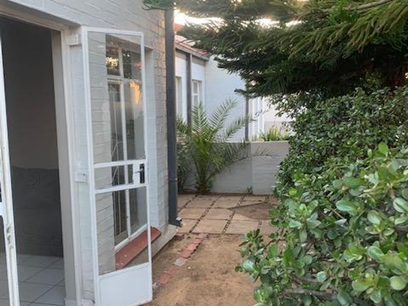 A view of the rear exterior area featuring a security gate, paved walkway, and established garden beds along the brick townhouse wall.