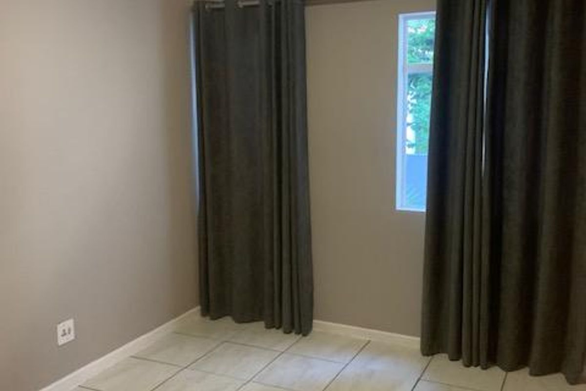 A clean, empty bedroom featuring neutral tiled flooring, simple wall finishes, and a window with installed curtain rods.