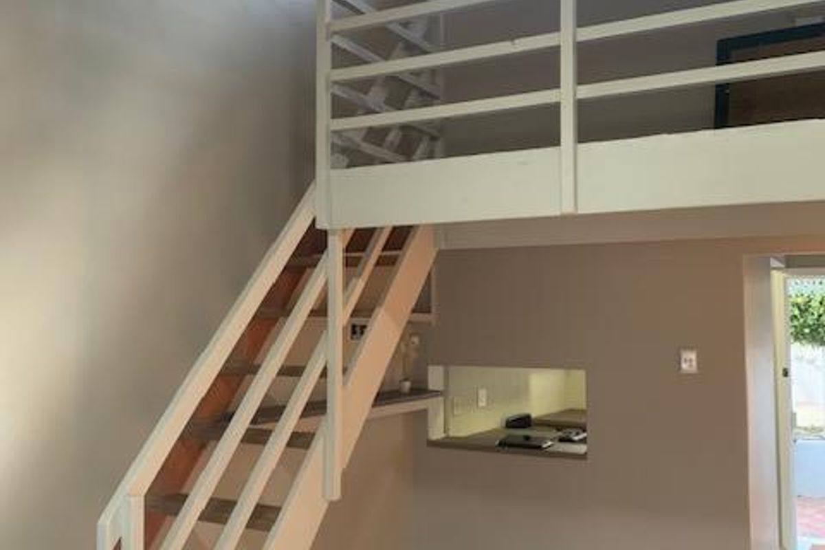 Open plan living area featuring a mezzanine level, exposed timber ceiling beams, and a staircase, with tiled flooring and a convenient pass-through window.