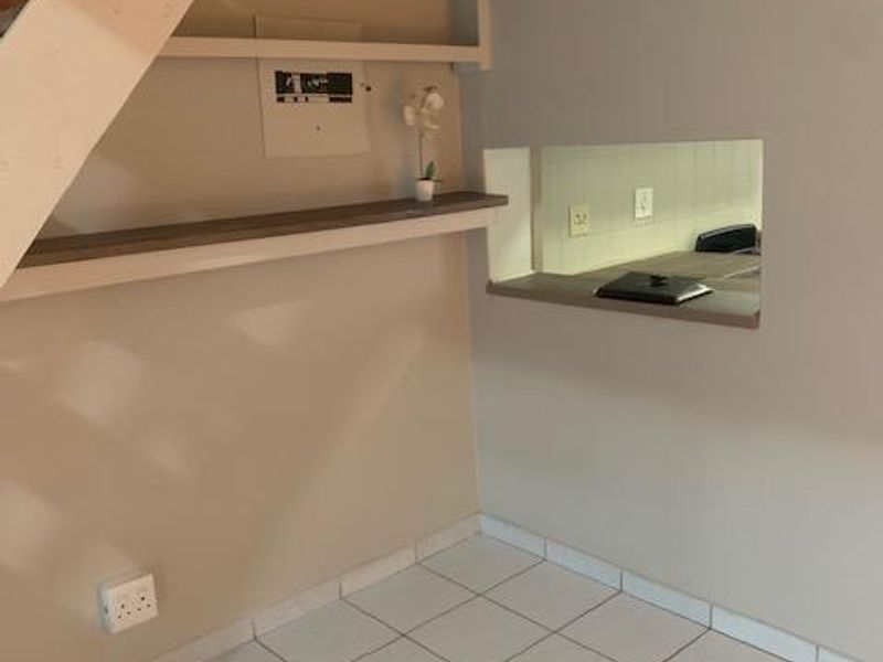 An empty living area featuring tiled flooring, a staircase, built-in shelving, and a serving hatch looking through to the kitchen area.