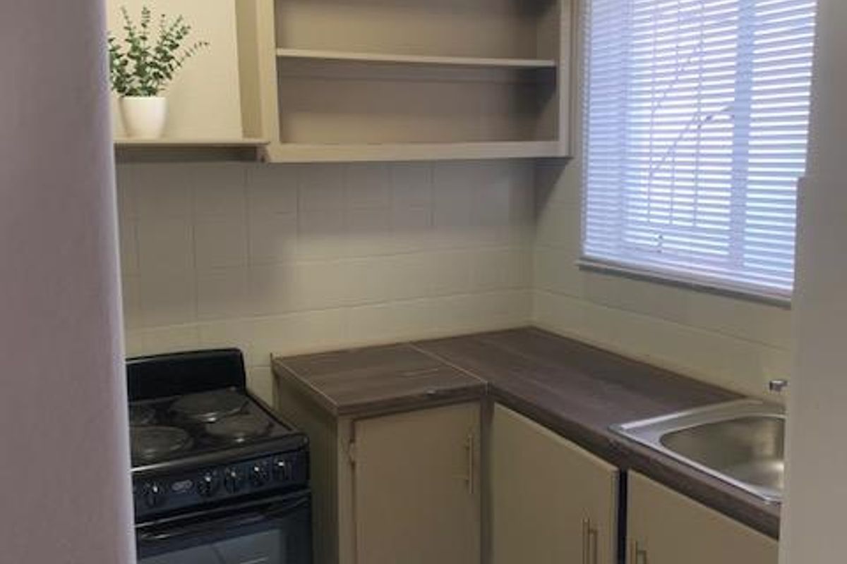 Compact kitchen featuring built-in cabinetry, laminate countertops, a stainless steel sink, and a freestanding stove with tiled backsplash and flooring.