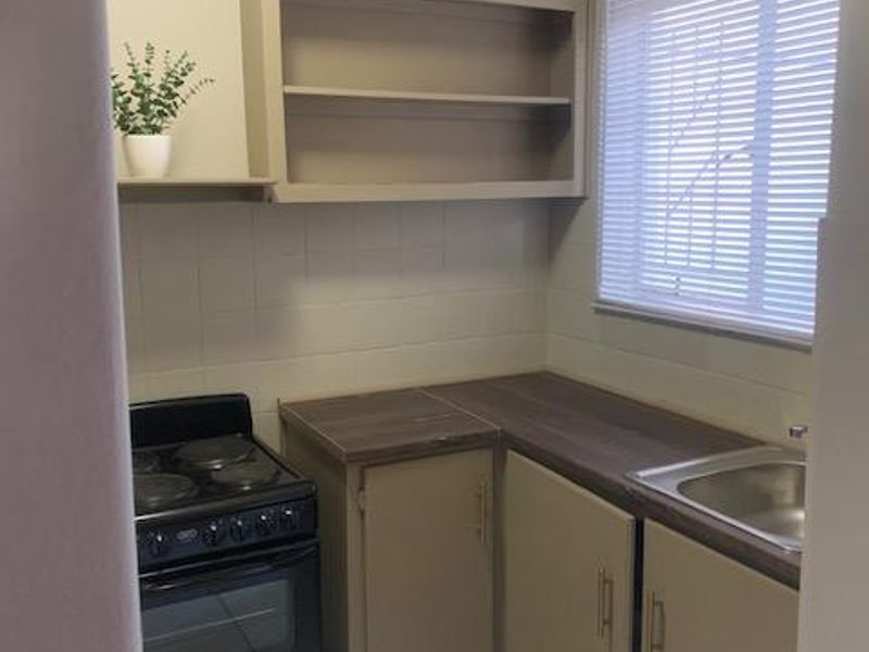 Compact kitchen featuring built-in cabinetry, laminate countertops, a stainless steel sink, and a freestanding stove with tiled backsplash and flooring.